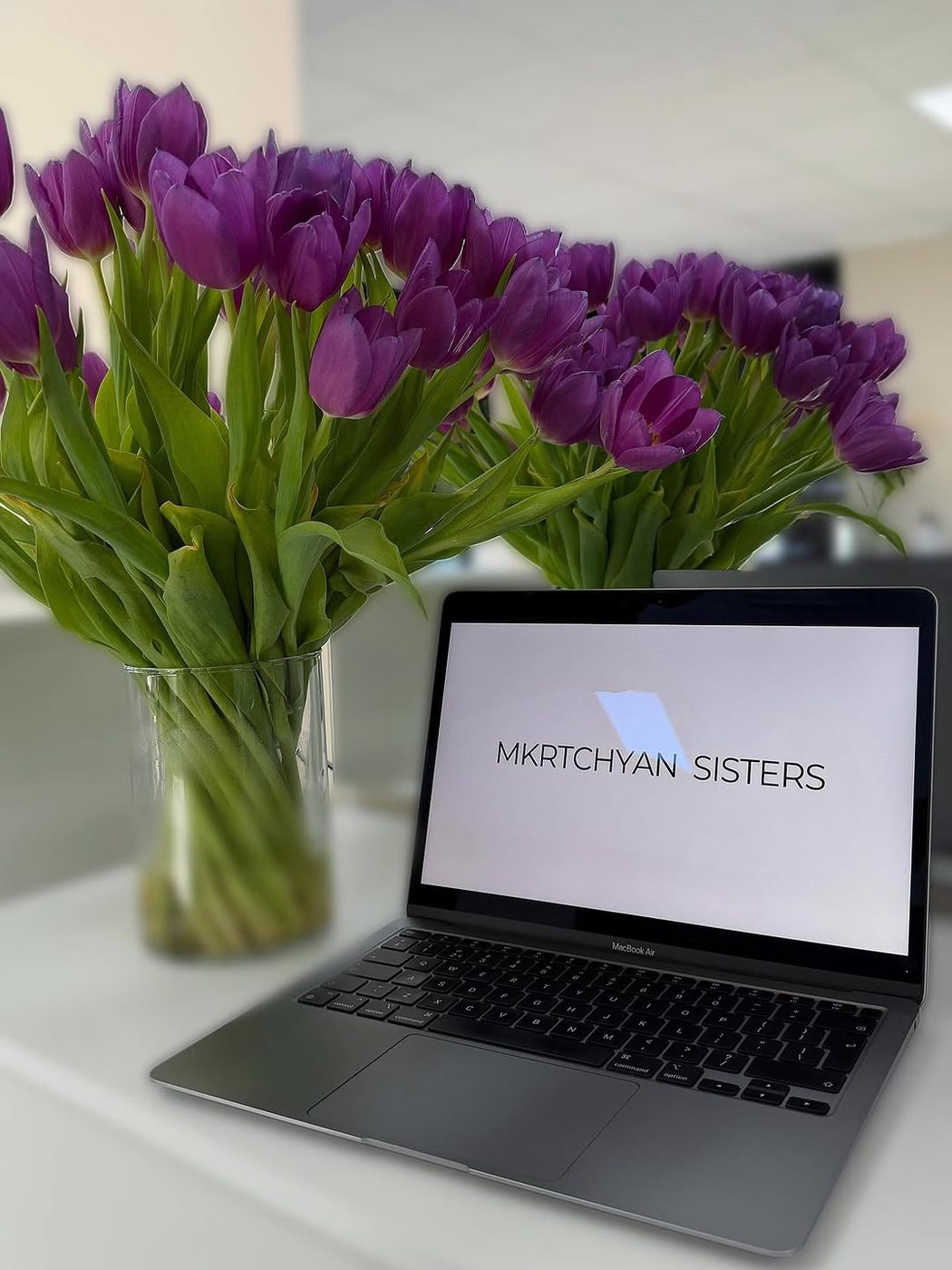 Paarse tulpen naast een laptop met het logo Mkrtchyan Sisters